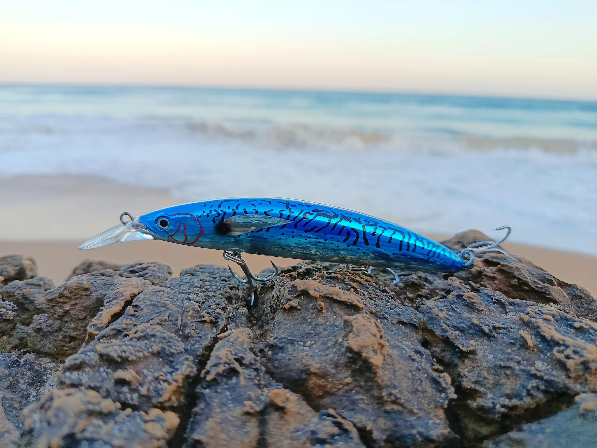 Blue fishing lure on rocky beach background.