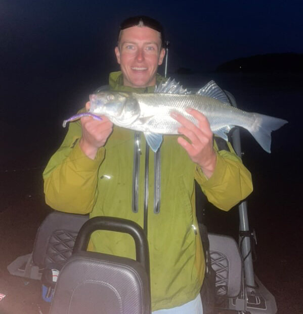 Person holding a fish at night on a boat.