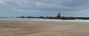 Sandy beach with distant tower under cloudy sky.