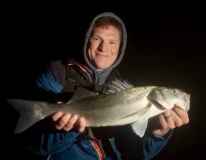 Person holding a large fish at night.